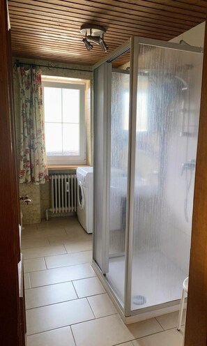 Un baño con ducha, un radiador y una ventana con cortinas.