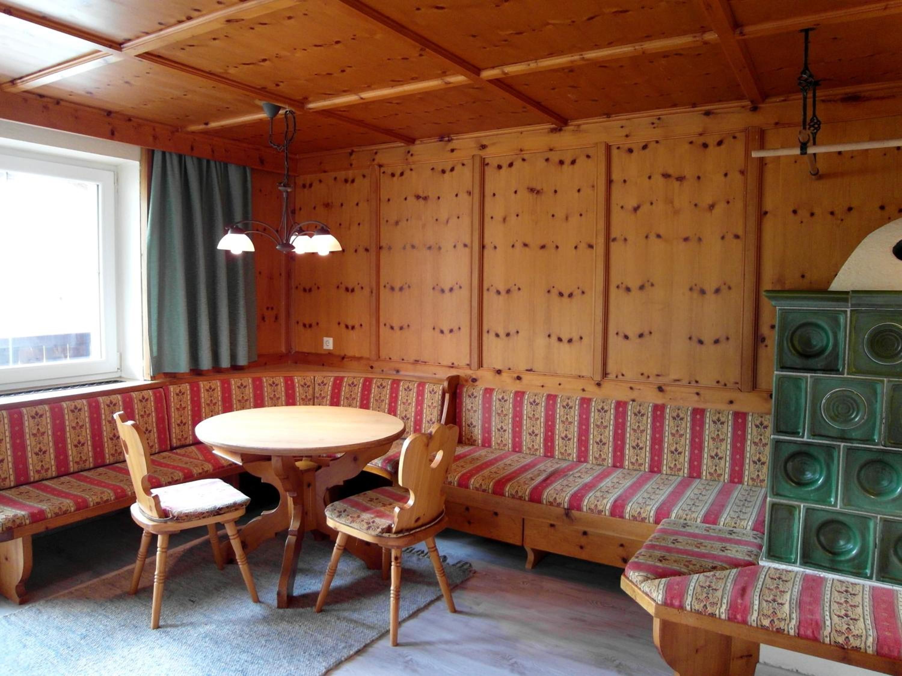 Interior de madera con una mesa redonda, dos sillas, un banco y un armario.