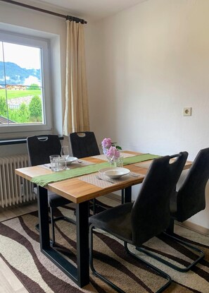 A dining area with a table set for two, chairs, a view of a mountain landscape, and a radiator. - Appartements Konrad (Soell)
