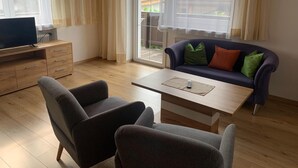En moderne stue med en sofa, to lænestole, et sofabord og et fjernsyn på et træskab.