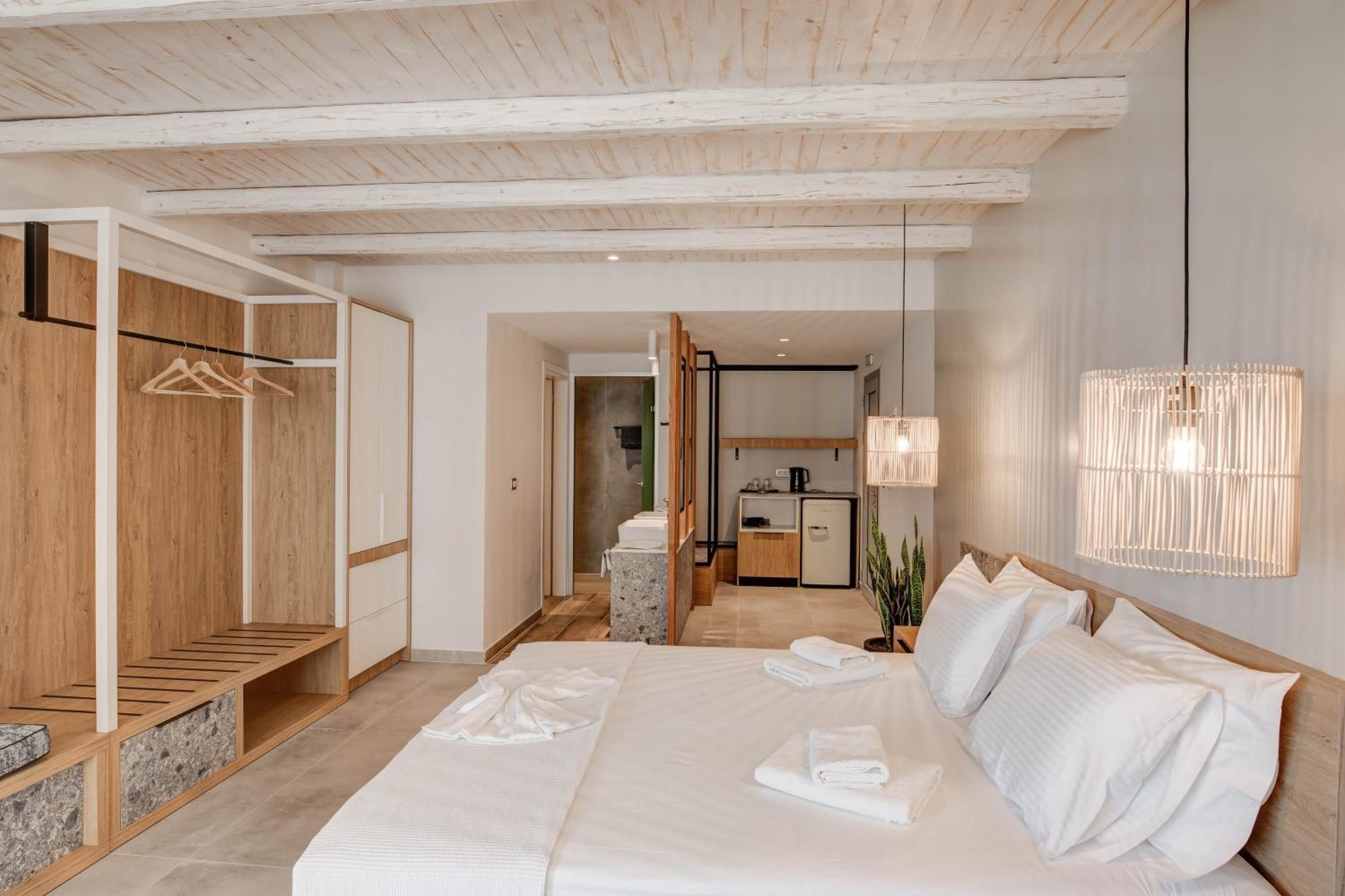 A hotel room with a large bed, a wooden bench, a wardrobe, and a kitchenette.