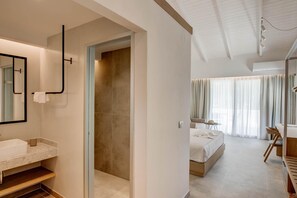 A modern hotel room with a bathroom, a walk-in closet, and a bedroom with a bed and a desk. - Alboro Seaside Suites (Parga)