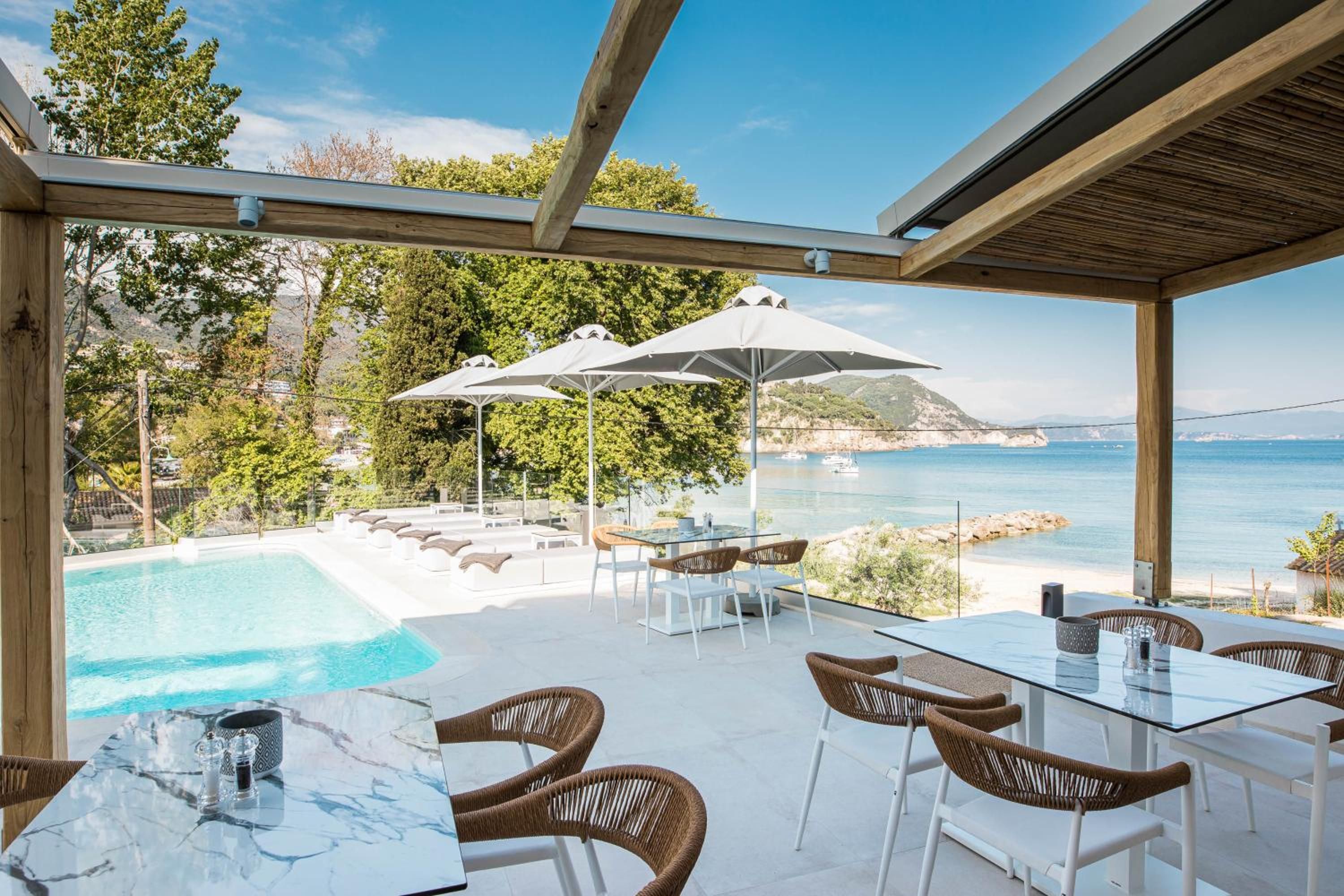 A poolside area with lounge chairs, a table, and umbrellas overlooking a body of water.