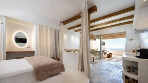 Une chambre moderne comprenant un lit, un miroir rond, un coin salon avec vue sur la mer et une kitchenette.