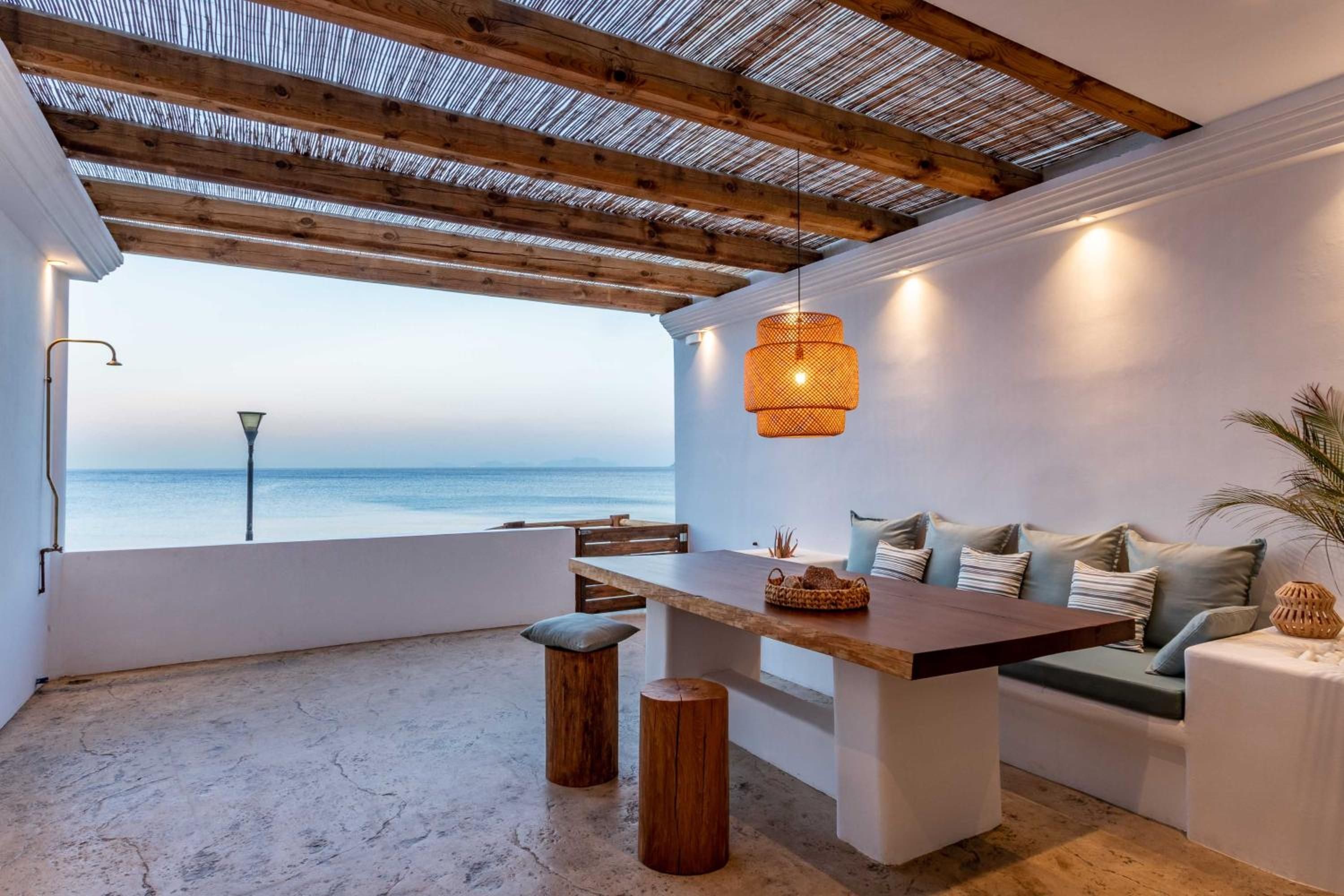 A modern interior with a wooden ceiling, a dining area with a table and benches, and a view of the sea.