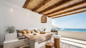 Un espace extérieur moderne, aménagé avec une table en bois, des coussins blancs et un luminaire tressé.