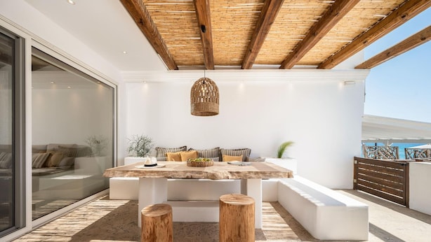 Un espace extérieur moderne, aménagé avec une table en bois, deux tabourets et un luminaire suspendu.