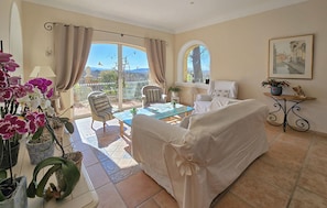 A sunlit room with a sofa, a table, and chairs, a window with a view, and a painting on the wall. - Stunning home in Robion (Robion)