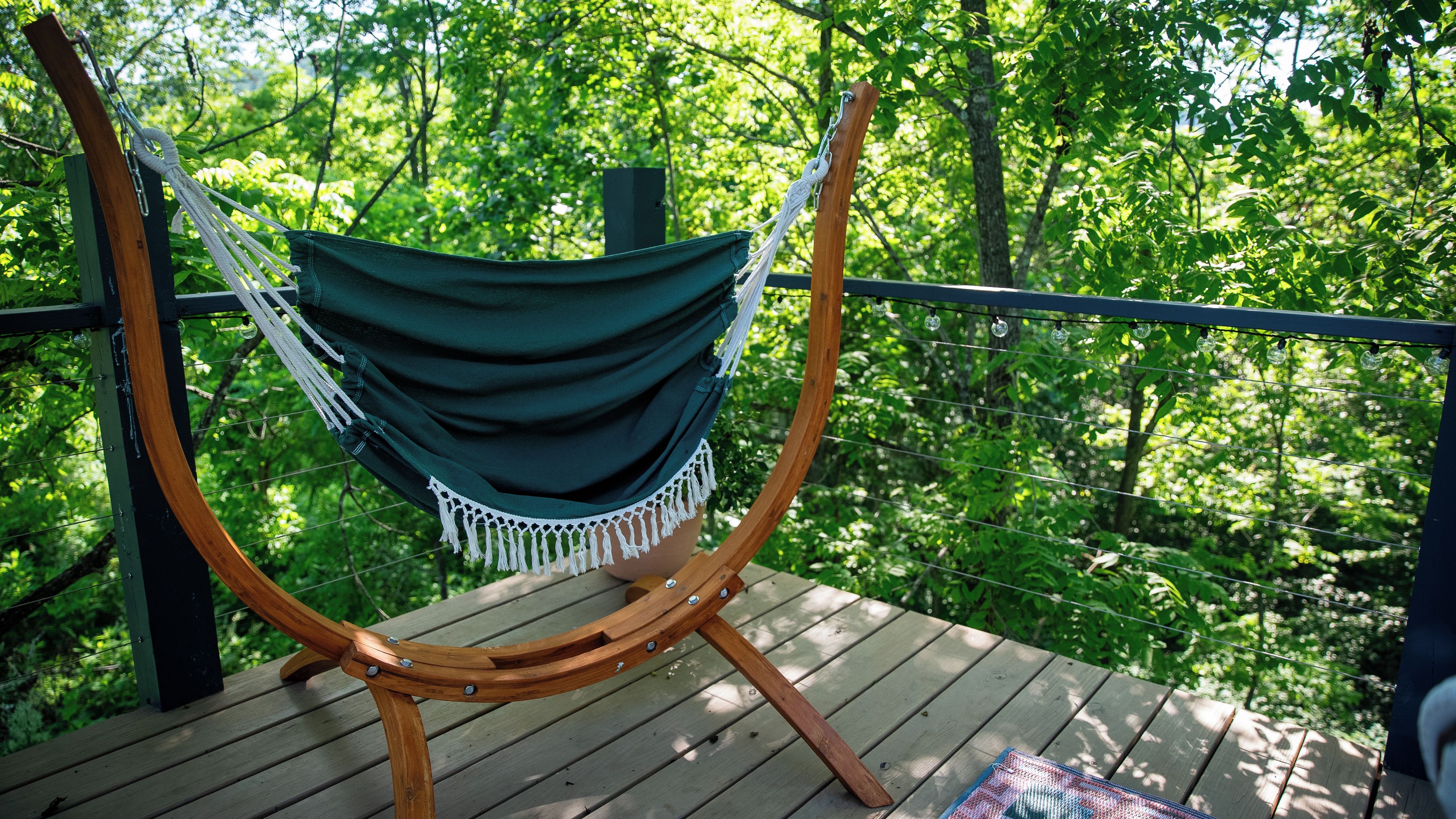 Un fauteuil suspendu, de type hamac, sur une terrasse en bois, avec vue sur une forêt.