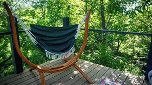 A hammock chair on a wooden deck with a view of a forest.