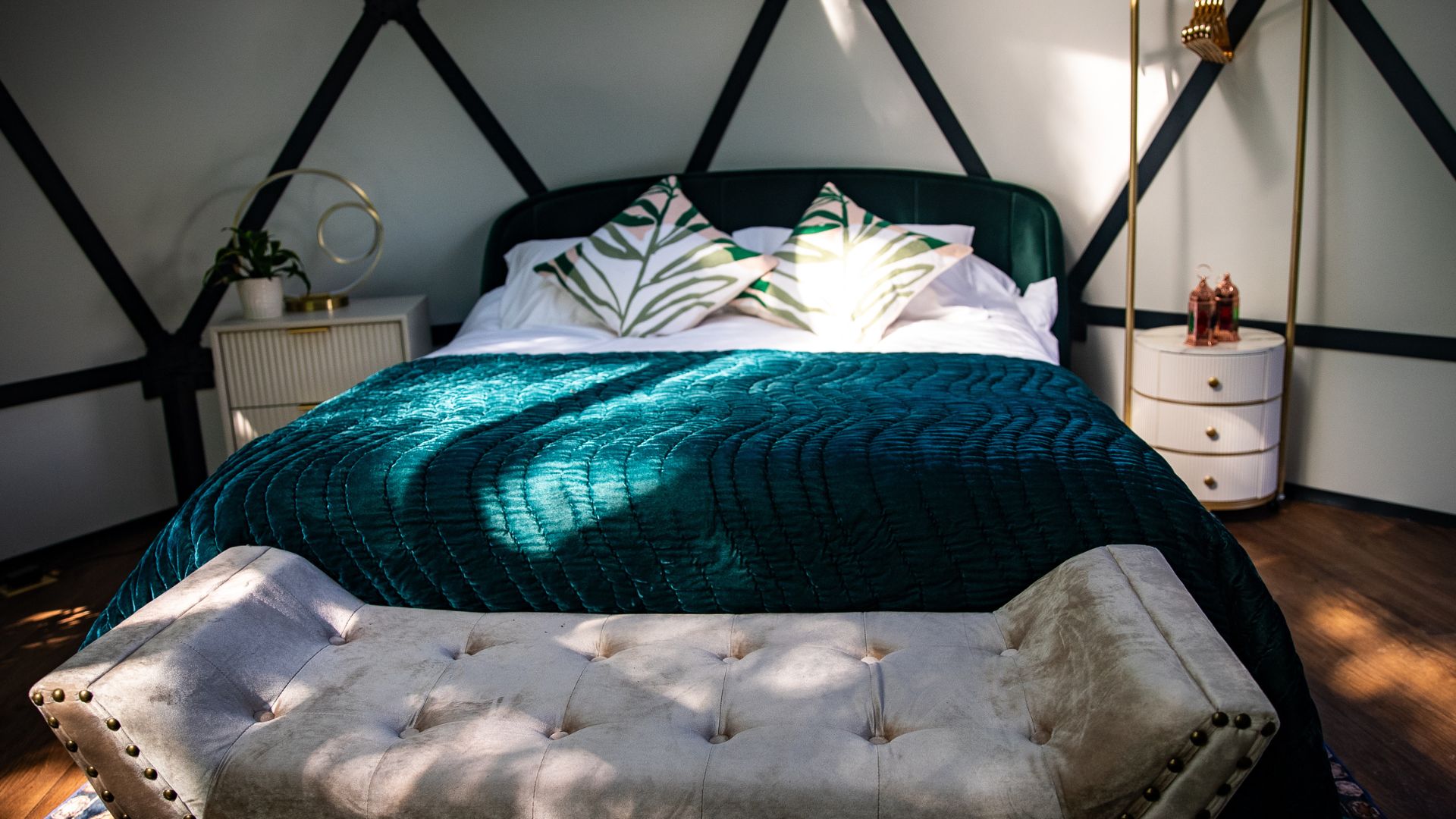 Un lit recouvert d’une courtepointe turquoise, un banc capitonné, une table de chevet avec une lampe et un mur orné d’un motif géométrique.