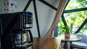 A coffee maker on a table with a window view.