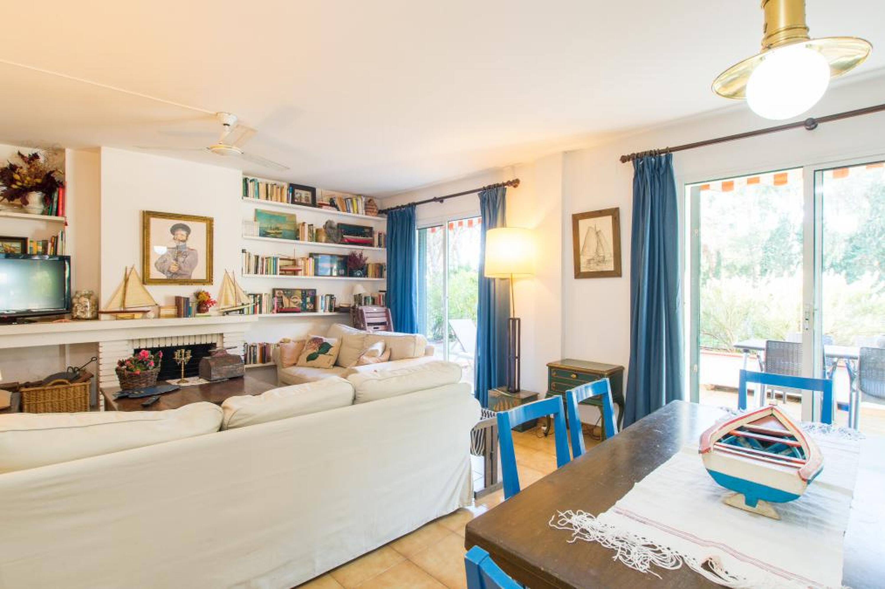 Un salon chaleureux avec un canapé, une cheminée, une bibliothèque et un coin repas comprenant une table et des chaises.
