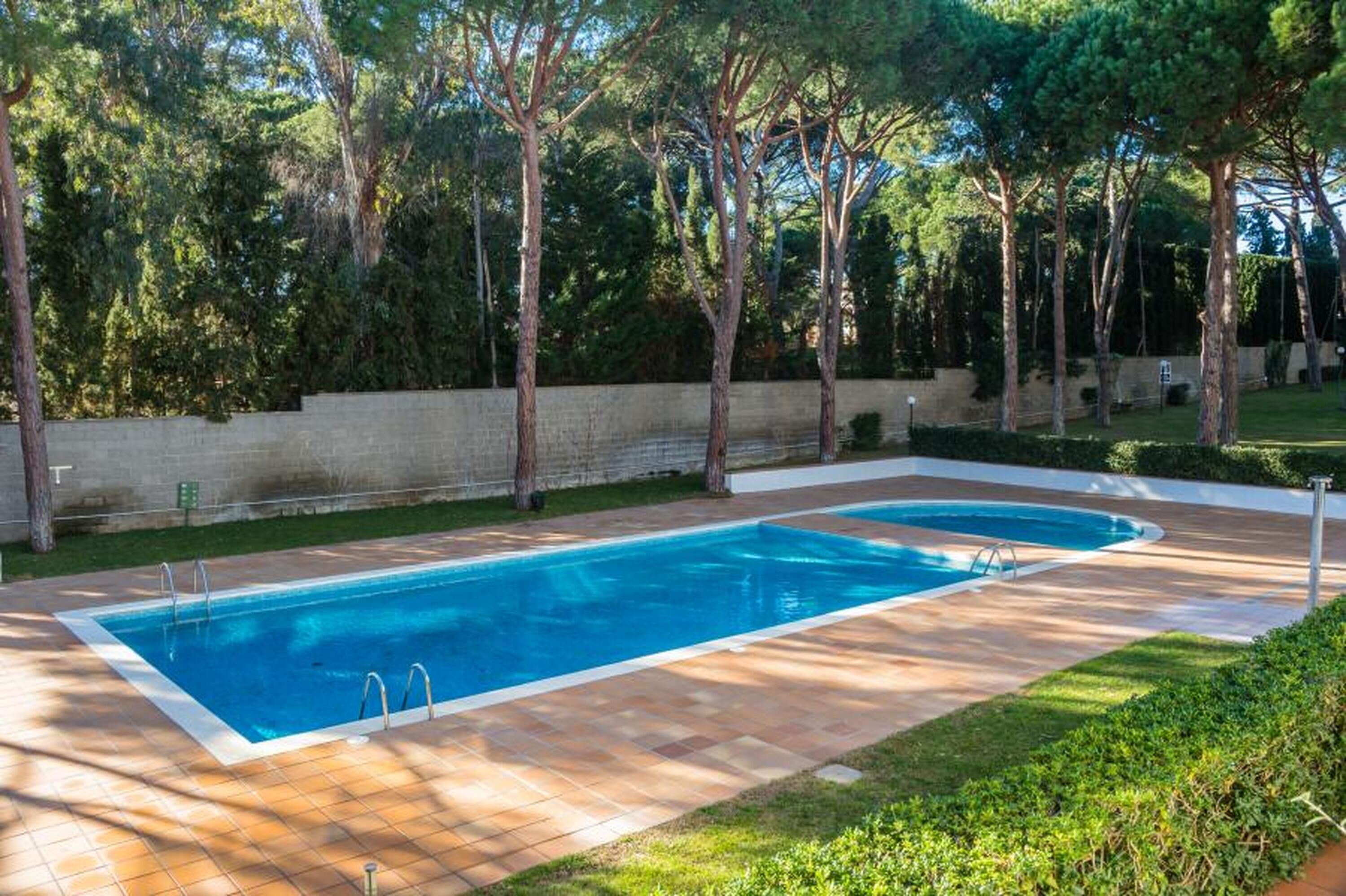 Una piscina rectangular con dos escaleras, rodeada por un patio de ladrillo y un muro de piedra bajo.