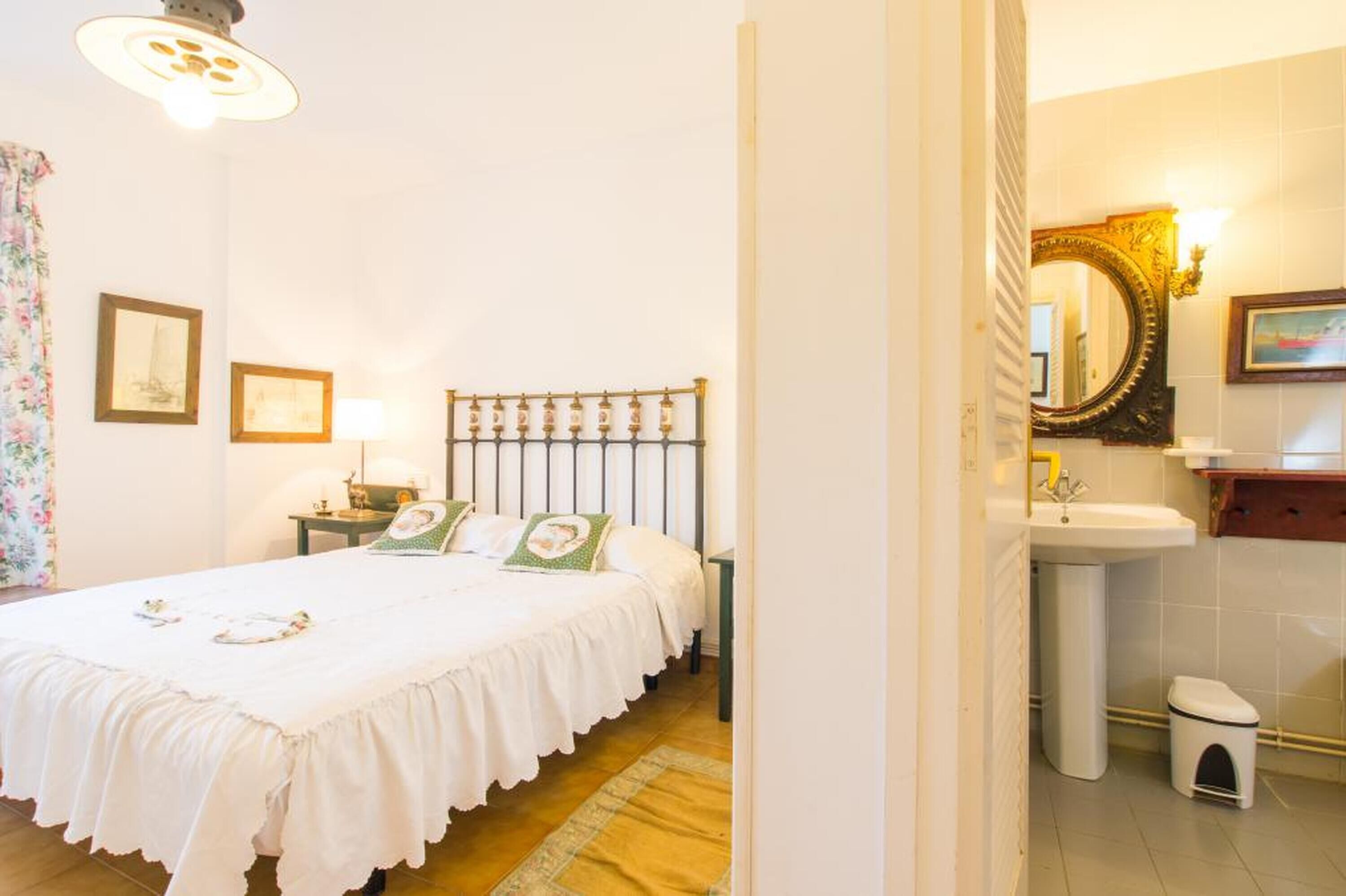 A hotel room with a bed, a nightstand, a lamp, a mirror, and a bathroom with a sink and toilet.