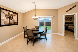 A dining area with a round table and chairs, a chandelier, and a large framed picture on the wall.