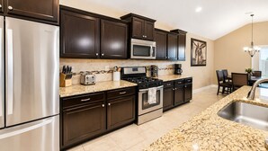 A modern kitchen with dark cabinetry, stainless steel appliances, granite countertops, and a large island with a sink.