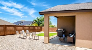 An outdoor patio area with a barbecue grill, seating, and a view of a backyard.