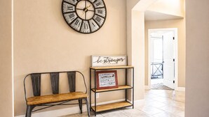A hallway with a wall-mounted clock, a bench, and a shelf with a motivational sign.