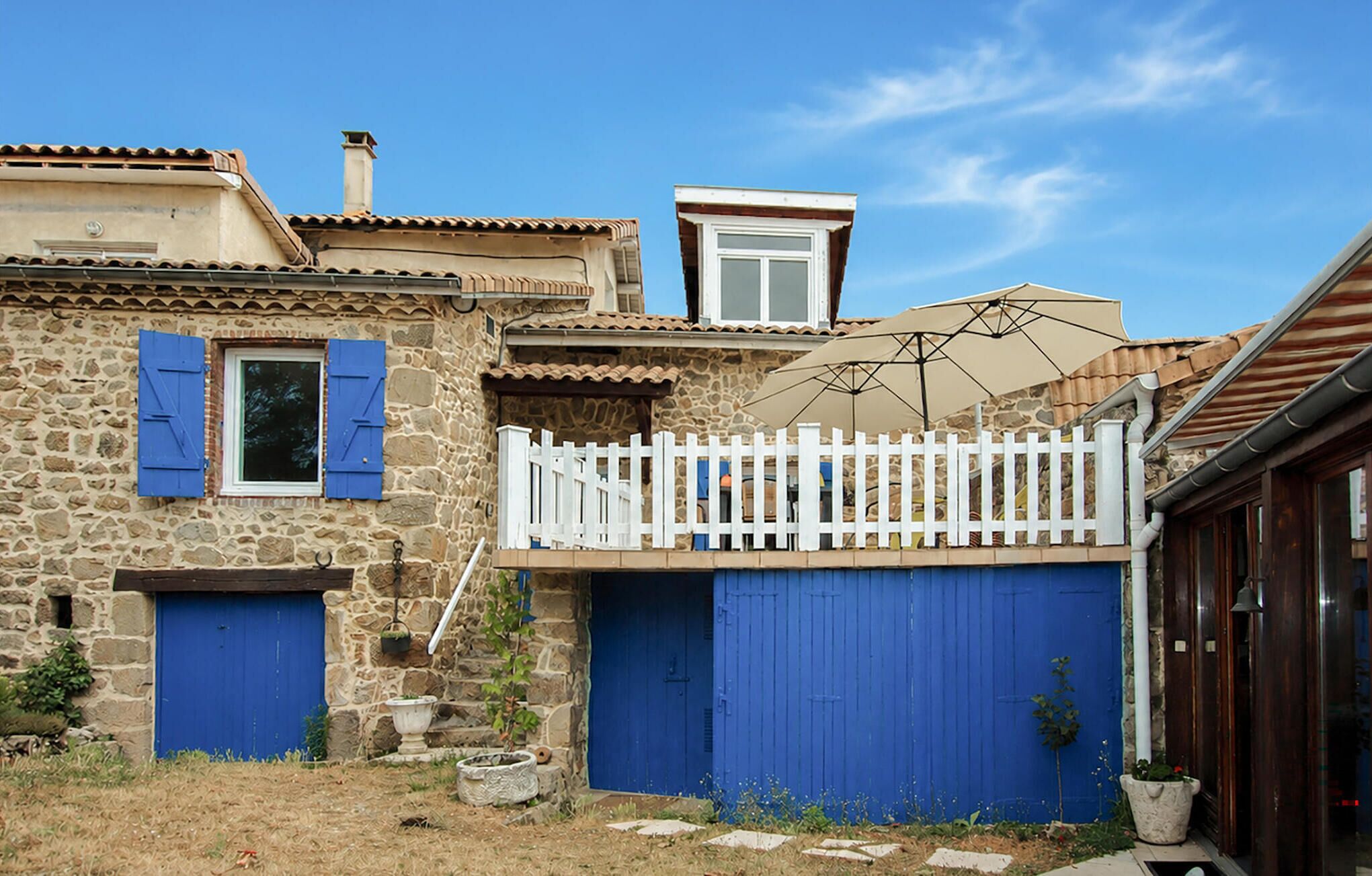 Un bâtiment en pierre avec une clôture blanche, des volets bleus et une grande porte de garage bleue.
