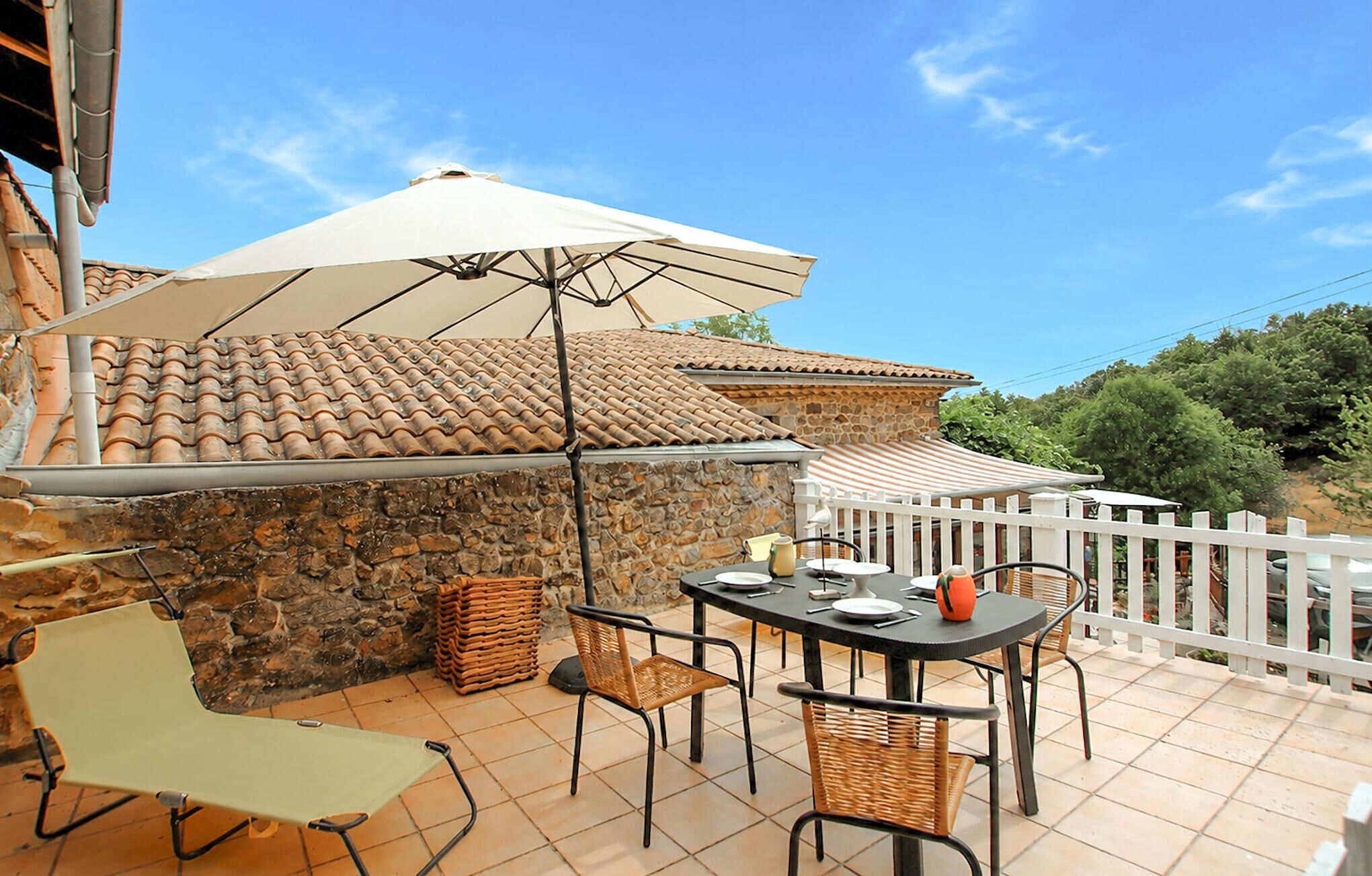 Eine Terrasse im Freien mit Tisch und Stühlen, einem weißen Sonnenschirm und einer Steinmauer.