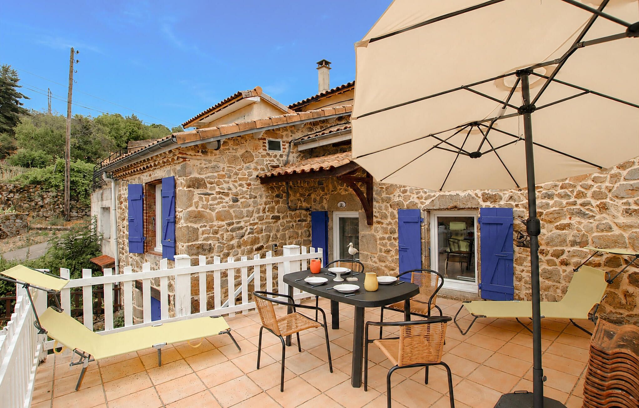 A stone building with a balcony, outdoor seating, and a white fence.