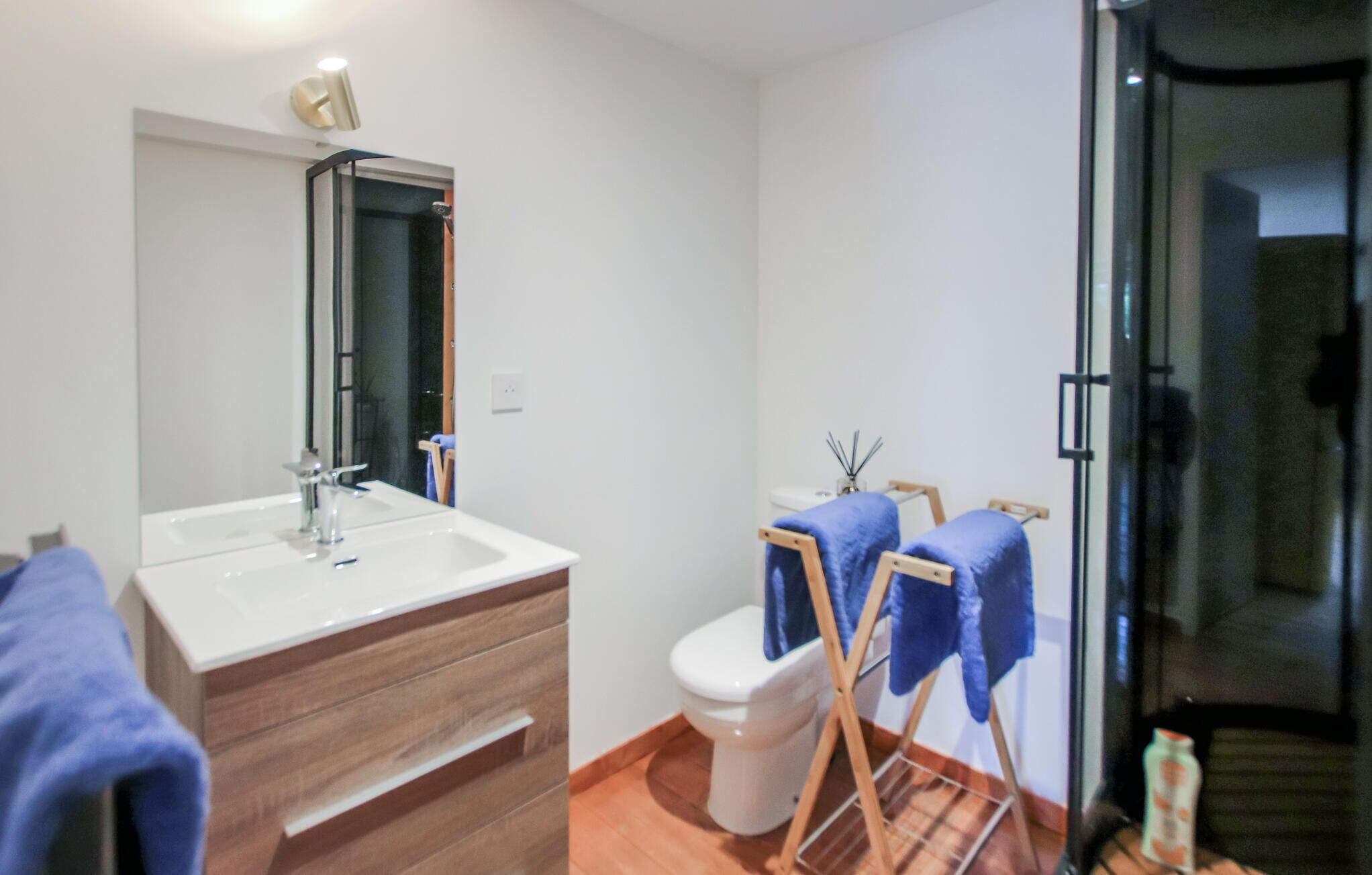 A bathroom with a white sink, mirror, and toilet. There are wooden towels on a rack and a glass shower door.