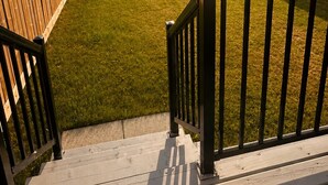 Un patio trasero cercado con zona de césped y terraza de madera.