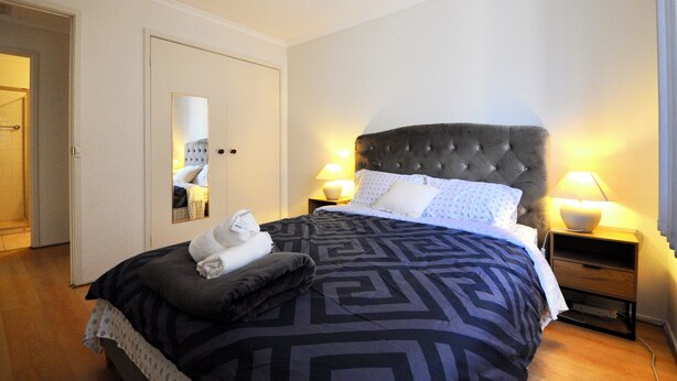 A hotel room with a large bed, two bedside lamps, a mirror, and a neatly made bed with towels. - Large, spacious group stay, quiet area with a private yard, central in Melb S/E (Glen Waverley)