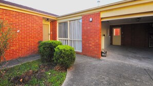 A two-story brick house with a garage, a small front yard with a bush, and a clear sky. - Large, spacious group stay, quiet area with a private yard, central in Melb S/E (Glen Waverley)