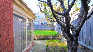 A backyard with a brick wall, a wooden fence, and a tree. - Large, spacious group stay, quiet area with a private yard, central in Melb S/E (Glen Waverley)