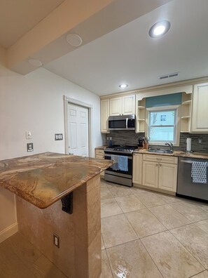 A kitchen with a marble countertop, stainless steel appliances, and beige cabinetry. - Coastal Escape - Backyard Oasis & Beach Vibes with Kayaks and Fitness Center (Ventnor City)