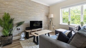 Una sala de estar moderna con un televisor de pantalla plana, una lámpara de pie y un sofá con cojines.