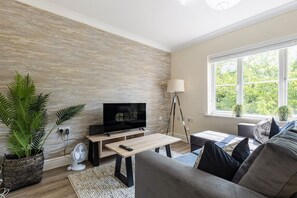 Ein modernes Wohnzimmer mit einem Flachbildfernseher, einer Stehlampe und einer Couch mit Kissen.