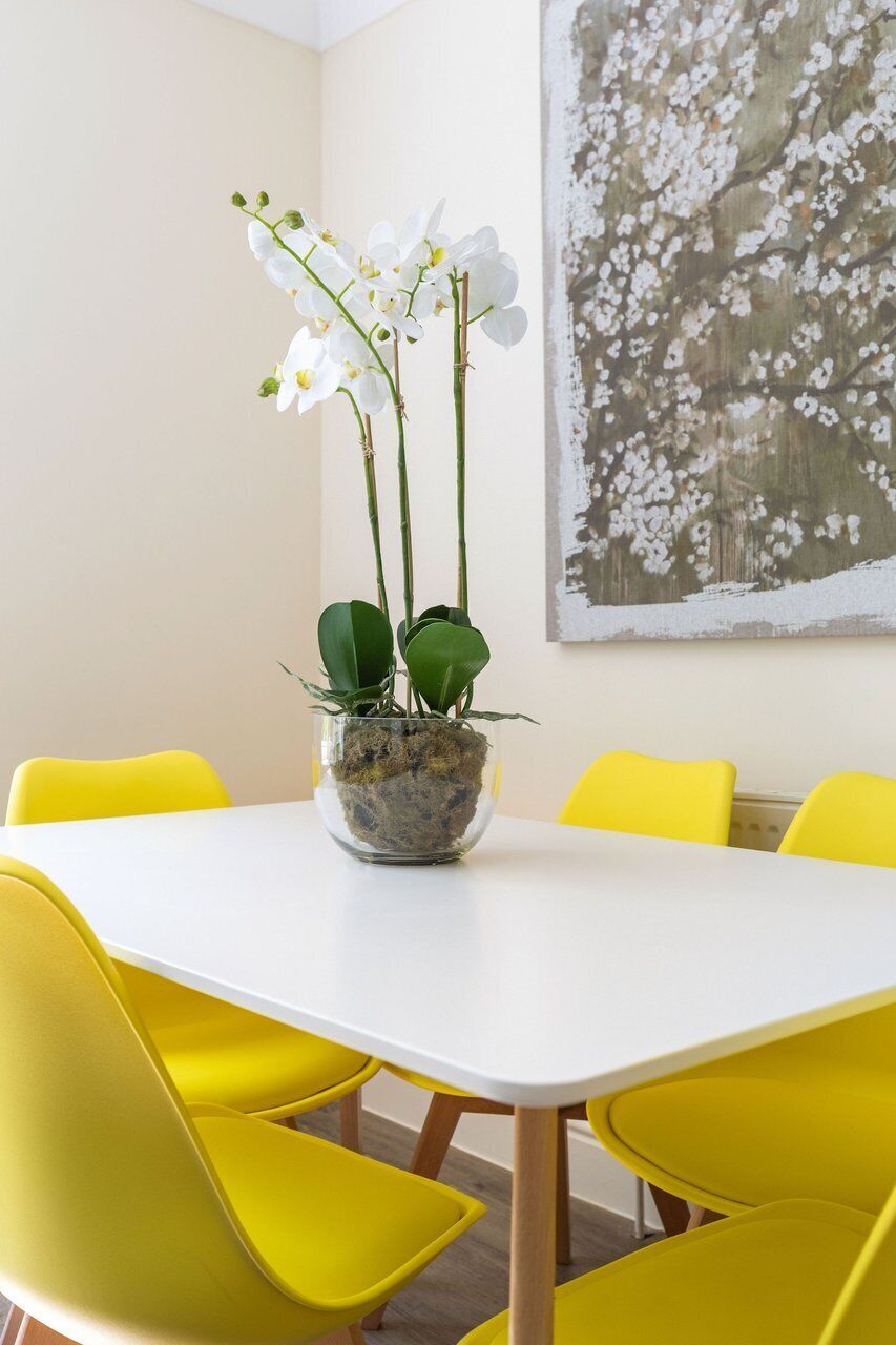 A dining table with a potted orchid plant, surrounded by yellow chairs.
