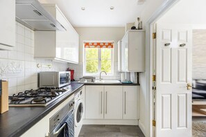 A kitchen with a gas stove, oven, microwave, and a washing machine. - GuestReady - Chic Retreat in Harrow (London)