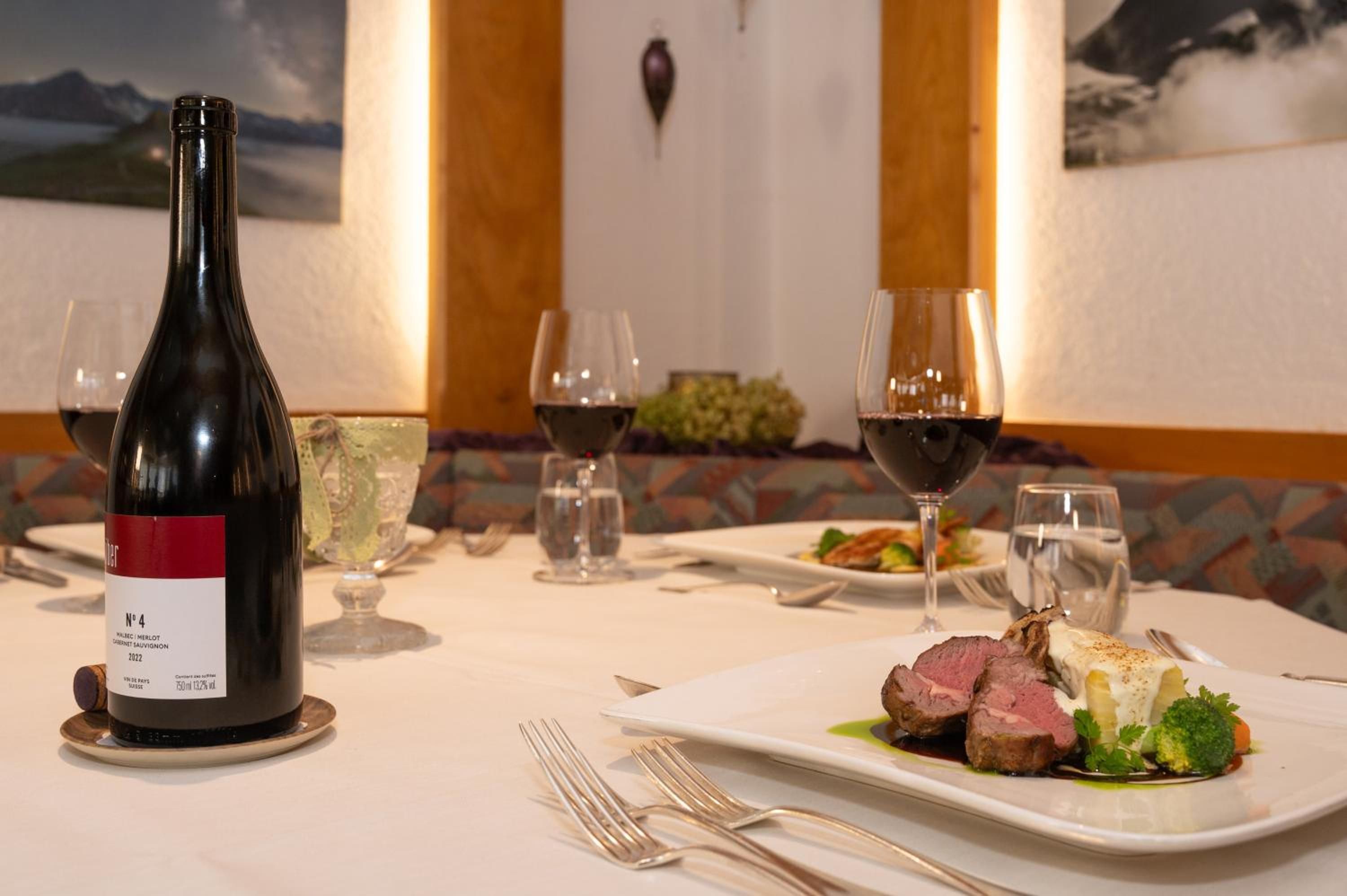 Una mesa de comedor dispuesta con una botella de vino, copas y un plato de comida.