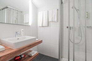 Un baño moderno con cabina de ducha de vidrio, un lavamanos blanco y un mueble de tocador de madera.