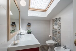 Un baño moderno con tragaluz, un lavamanos blanco, un inodoro y baldosas con diseño.