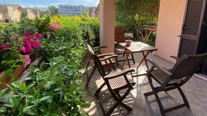 A covered outdoor patio with a table and chairs, surrounded by lush greenery and flowering plants. - B&b L'ulivo Fiumicino (Fiumicino)