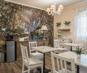A dining area with white chairs and tables, a chandelier, and a wall mural. - B&b L'ulivo Fiumicino (Fiumicino)