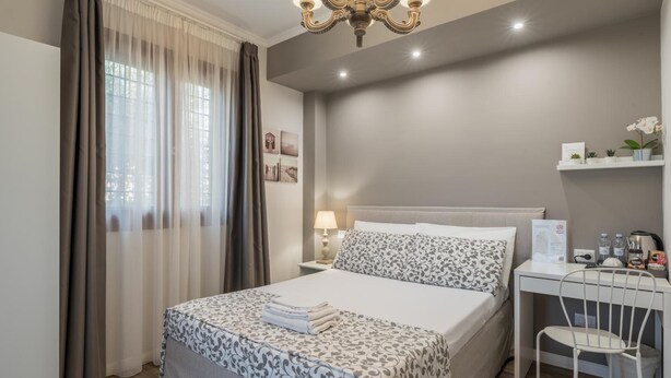 A neatly arranged hotel room with a bed, bedside table, lamp, and a small desk with a chair. - B&b L'ulivo Fiumicino (Fiumicino)