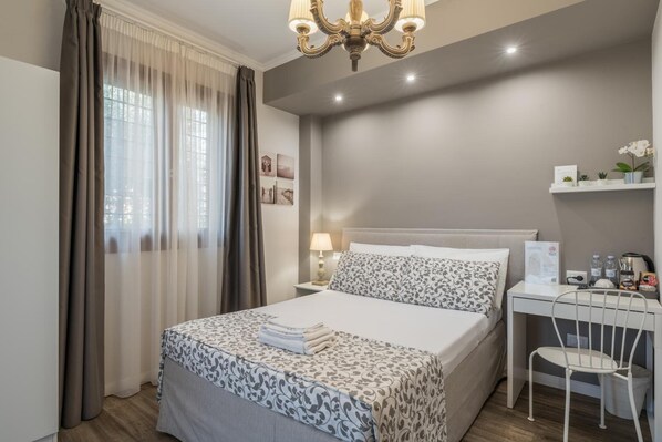 A neatly arranged hotel room with a bed, bedside table, lamp, and a small desk with a chair. - B&b L'ulivo Fiumicino (Fiumicino)