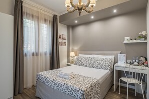 Habitación de hotel ordenada con cama, mesita de noche, lámpara y un pequeño escritorio con silla.
