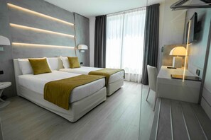Quarto de hotel moderno com duas camas, uma escrivaninha, uma cadeira e uma TV.
