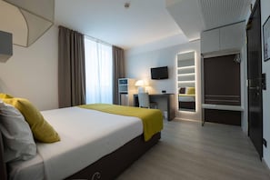 Quarto de hotel com uma cama, uma escrivaninha, uma televisão e um guarda-roupa.