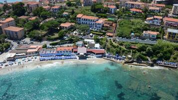 Una vista aerea di una cittadina costiera con spiaggia, edifici e acque blu cristalline.