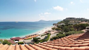 A coastal view with terracotta roofs, a beach, and a distant hill with buildings. - Hotel Villa Ombrosa (Portoferraio)