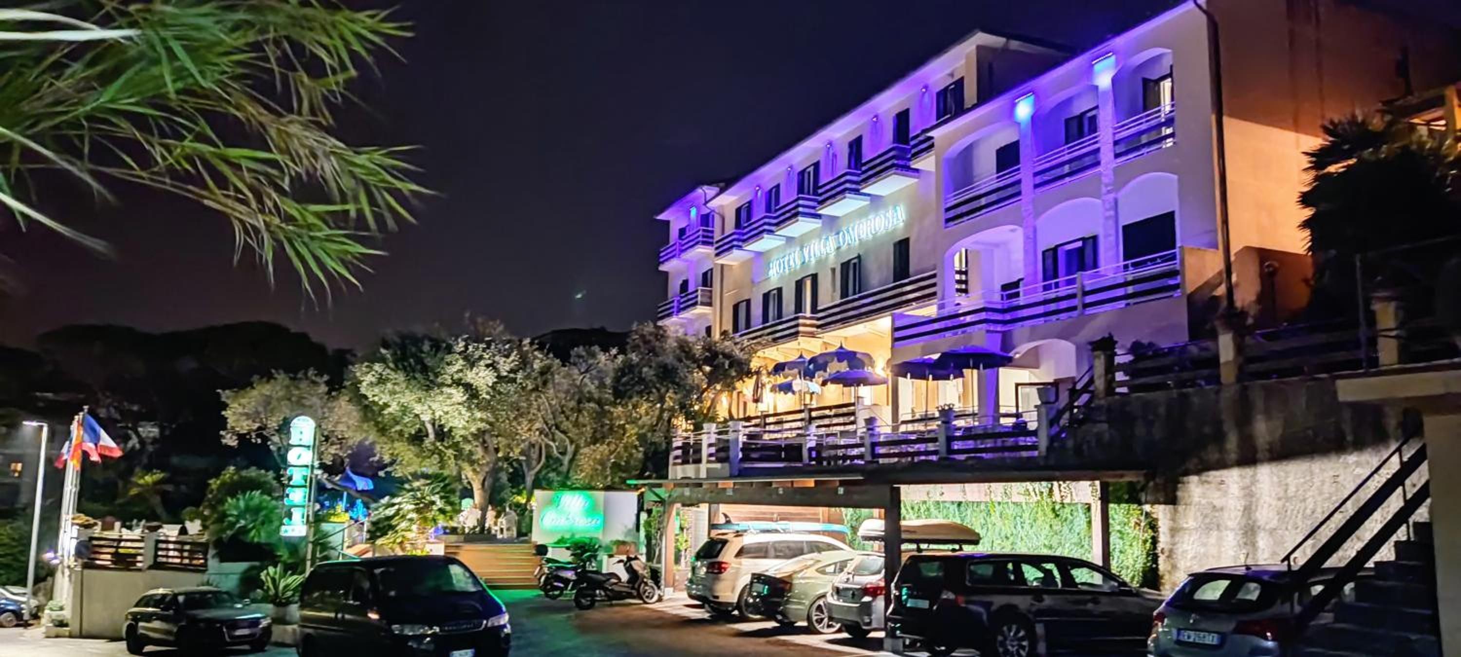 A multi-story hotel with a prominent sign, a covered outdoor seating area, and several parked cars.