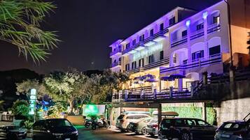 A multi-story hotel with a prominent sign, a covered outdoor seating area, and several parked cars.